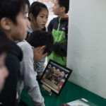 De jeunes fans de Chihayafuru observent la photo de l'équipe du film au centre de karuta du sanctuaire Ômi